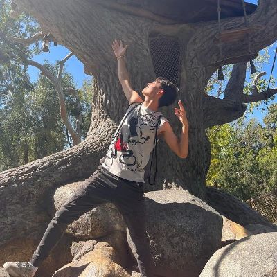 Max Torina is posing with his hands open as he is wearing a sleeveless shirt with Mickey mouse in it.